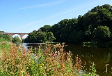 Picturesque photograph of Cumbria scenery, with river, trees and bridge in the distance