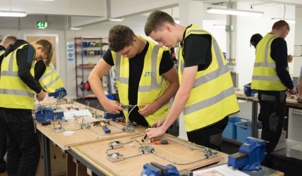 Photo of skilled workers in high visibility jackets constructing items on a workbench