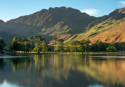 Photograph of Cumbria countryside with trees, hills and a serene lake.